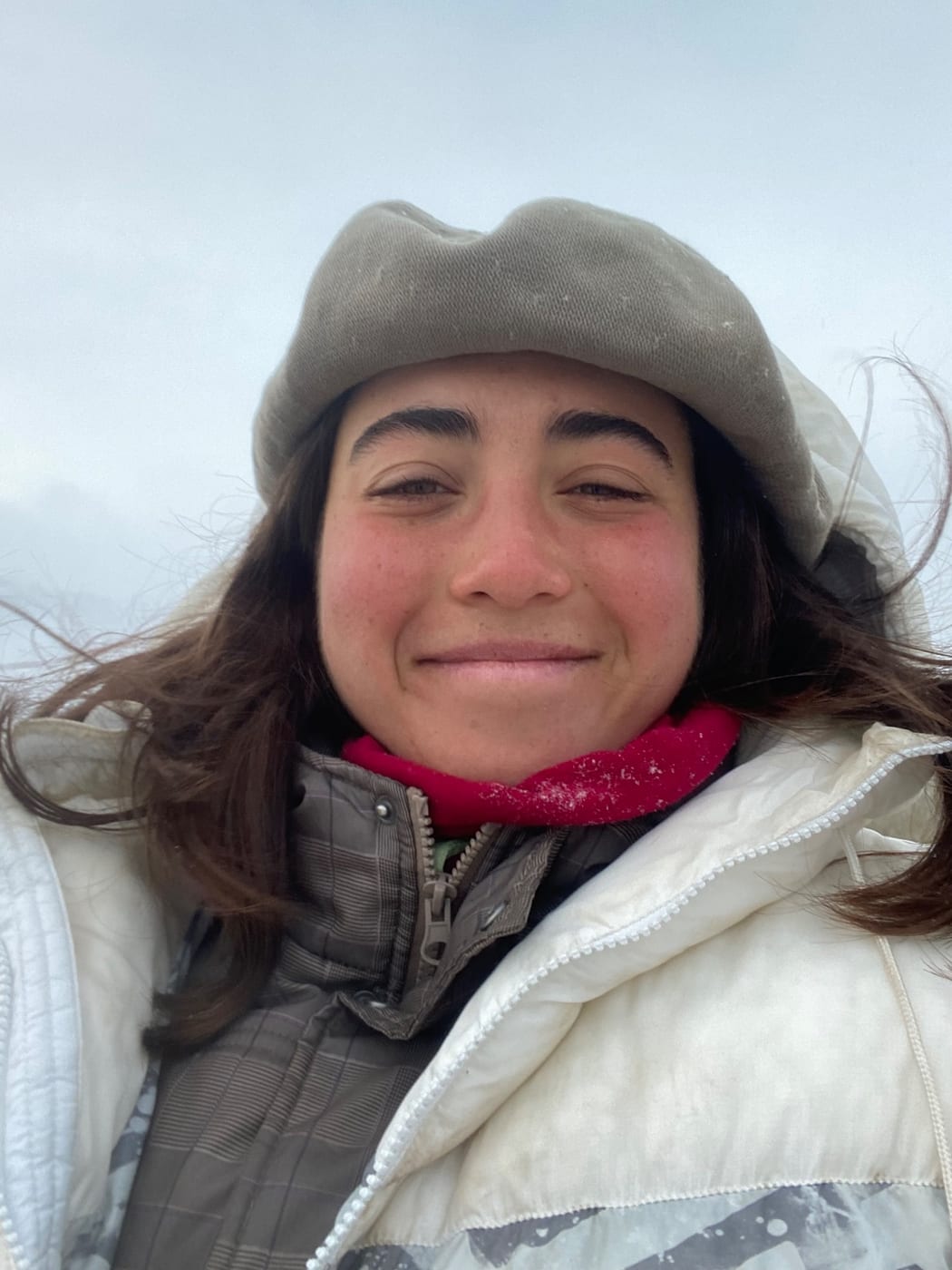 A smiling volunteer in a wool hat and white down jacket, in the mist