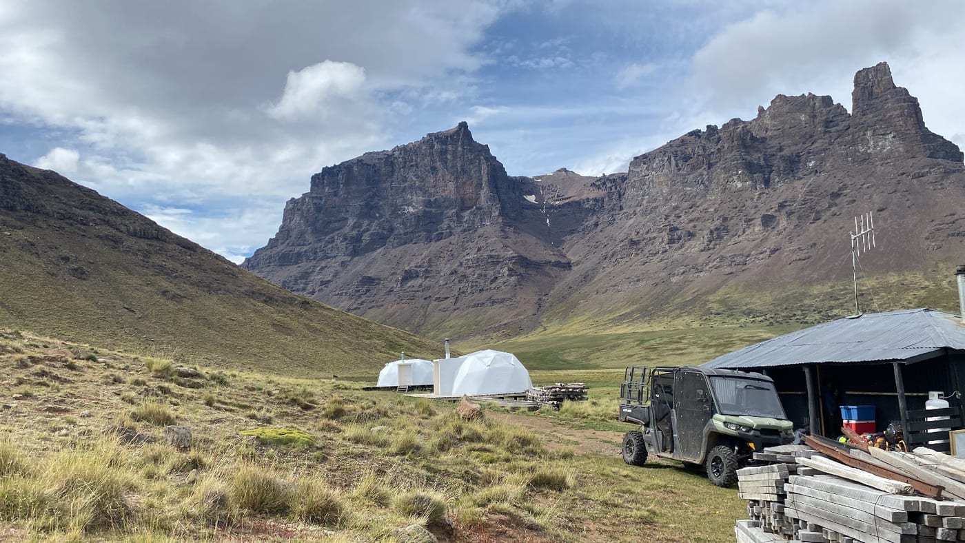White dome tents and a 4x4 utility vehicle in a valley beneath rock peaks