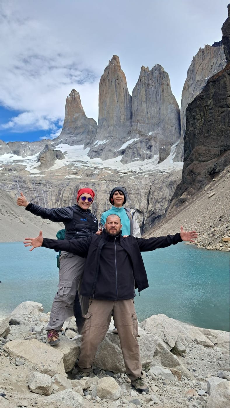 A family with their arms wide open in front of the Torres del Paine towers and a turquoise lake