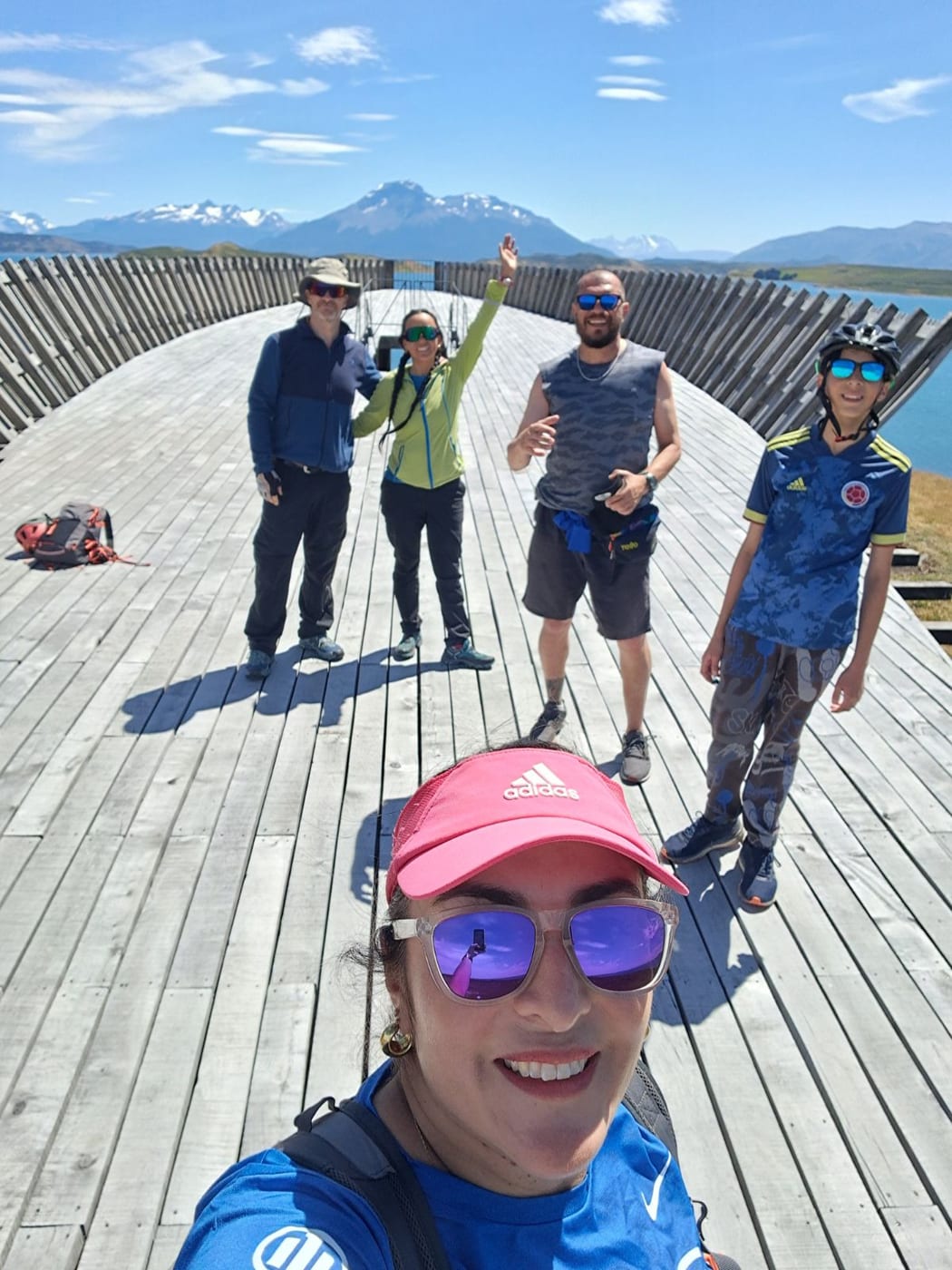 A group selfie on a curved wooden lookout above the water, with mountains behind