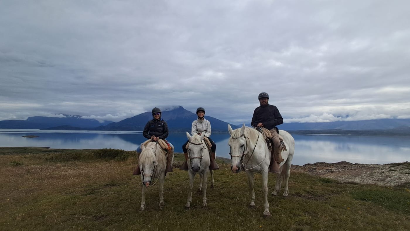 Three riders on white horses beside a still lake