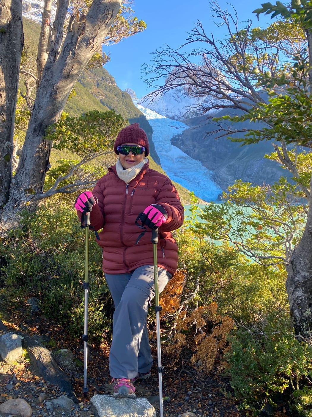 A guest on a forest trail with trekking poles, with a blue glacier behind her