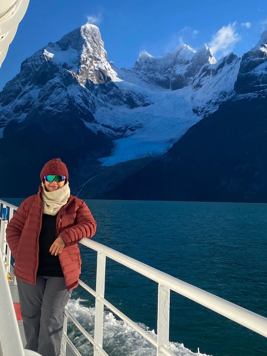 A guest on the deck of a boat, with snow-covered peaks and a glacier behind her