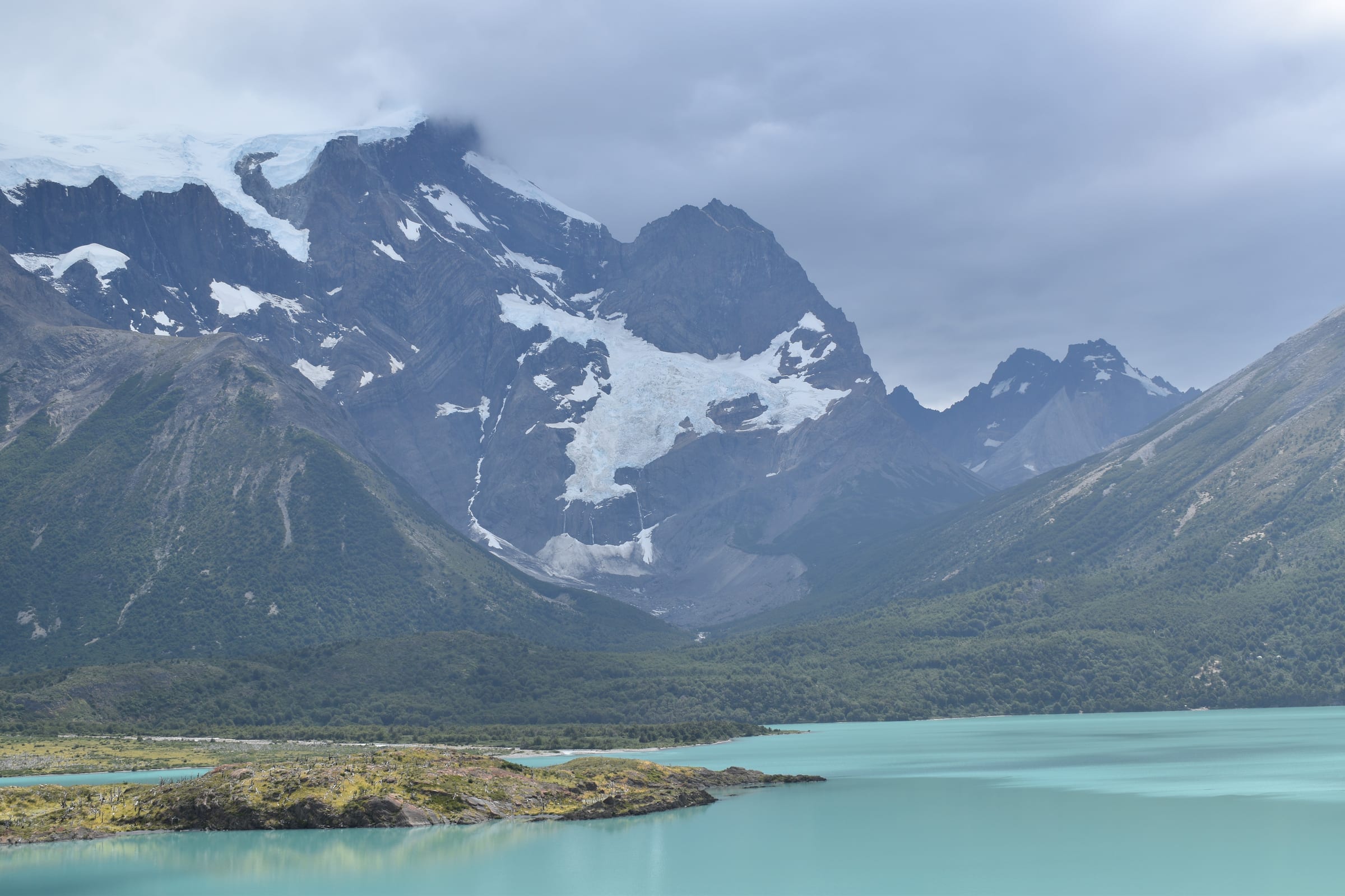 A glacier hanging from a cloud-covered mountain above a turquoise lake
